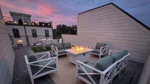 Un patio esterno con arredi bianchi, un braciere e vista su un edificio sullo sfondo.
