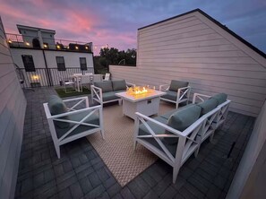Une terrasse extérieure avec des meubles blancs, un foyer et une vue sur un bâtiment en arrière-plan.