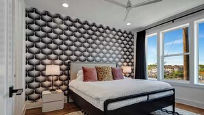 Una camera da letto moderna con carta da parati fantasia, un letto grande con molti cuscini, comodini e vista sull'esterno attraverso ampie finestre.