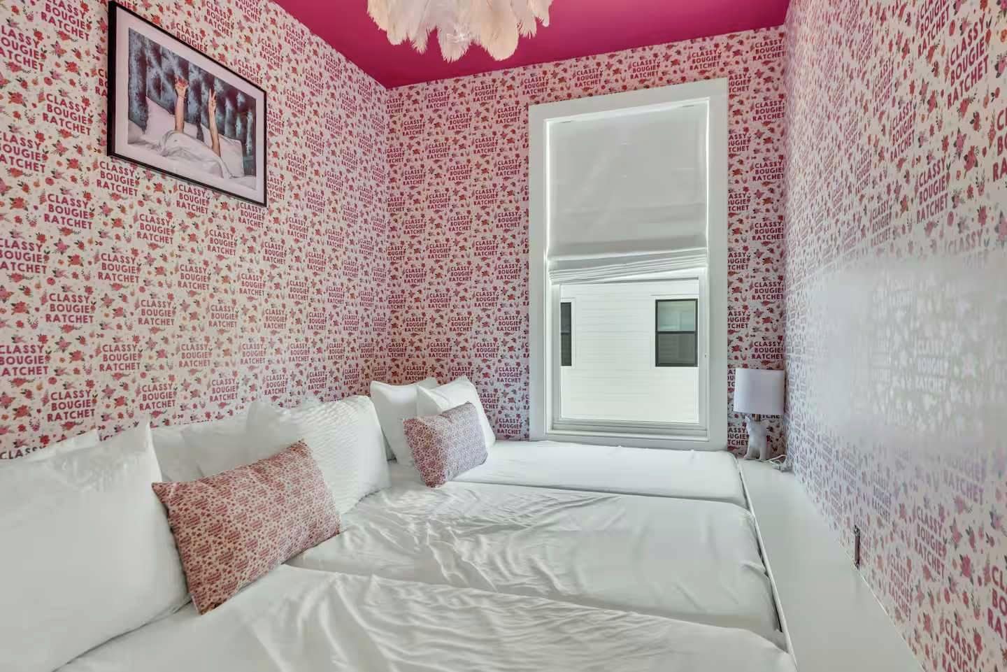 Un dormitorio con cama blanca, paredes rosadas y ventana con vistas.