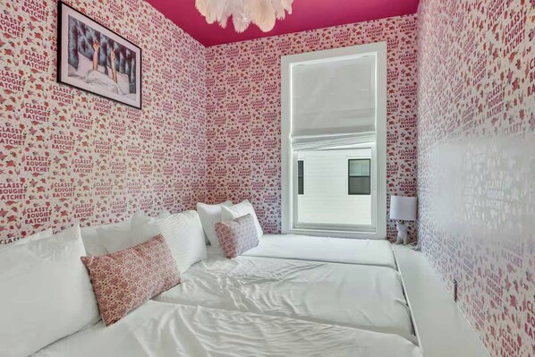 A bedroom with a white bed, pink walls, and a window with a view.