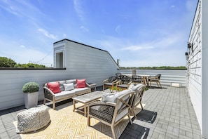 Une terrasse sur le toit, aménagée avec du mobilier d’extérieur, un pot de fleurs et offrant une vue sur le ciel.