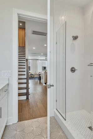 A modern bathroom with a glass shower enclosure and a wooden staircase leading to a living area.