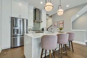 Whip up delicious group meals in this stunning white gourmet kitchen featuring sleek quartz countertops, a large island, and chic seating.
