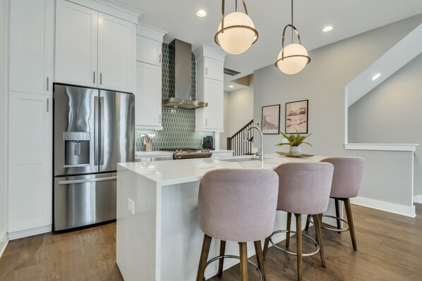Whip up delicious group meals in this stunning white gourmet kitchen featuring sleek quartz countertops, a large island, and chic seating.