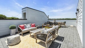A rooftop patio with outdoor furniture, a potted plant, and a view of the sky.