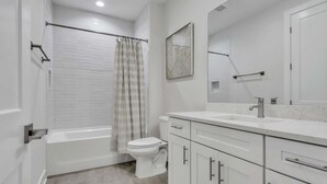 Un baño moderno con bañera, inodoro y tocador con cajones y espejo.