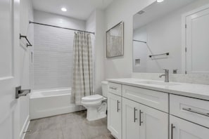 Une salle de bain moderne équipée d’une baignoire, de toilettes et d’un meuble-lavabo avec des tiroirs et un miroir.