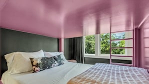 Un dormitorio con cama, ventana con cortinas y vista a zonas verdes.