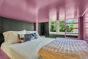 Une chambre à coucher avec un lit, une fenêtre avec des rideaux et une vue sur la verdure à l’extérieur.