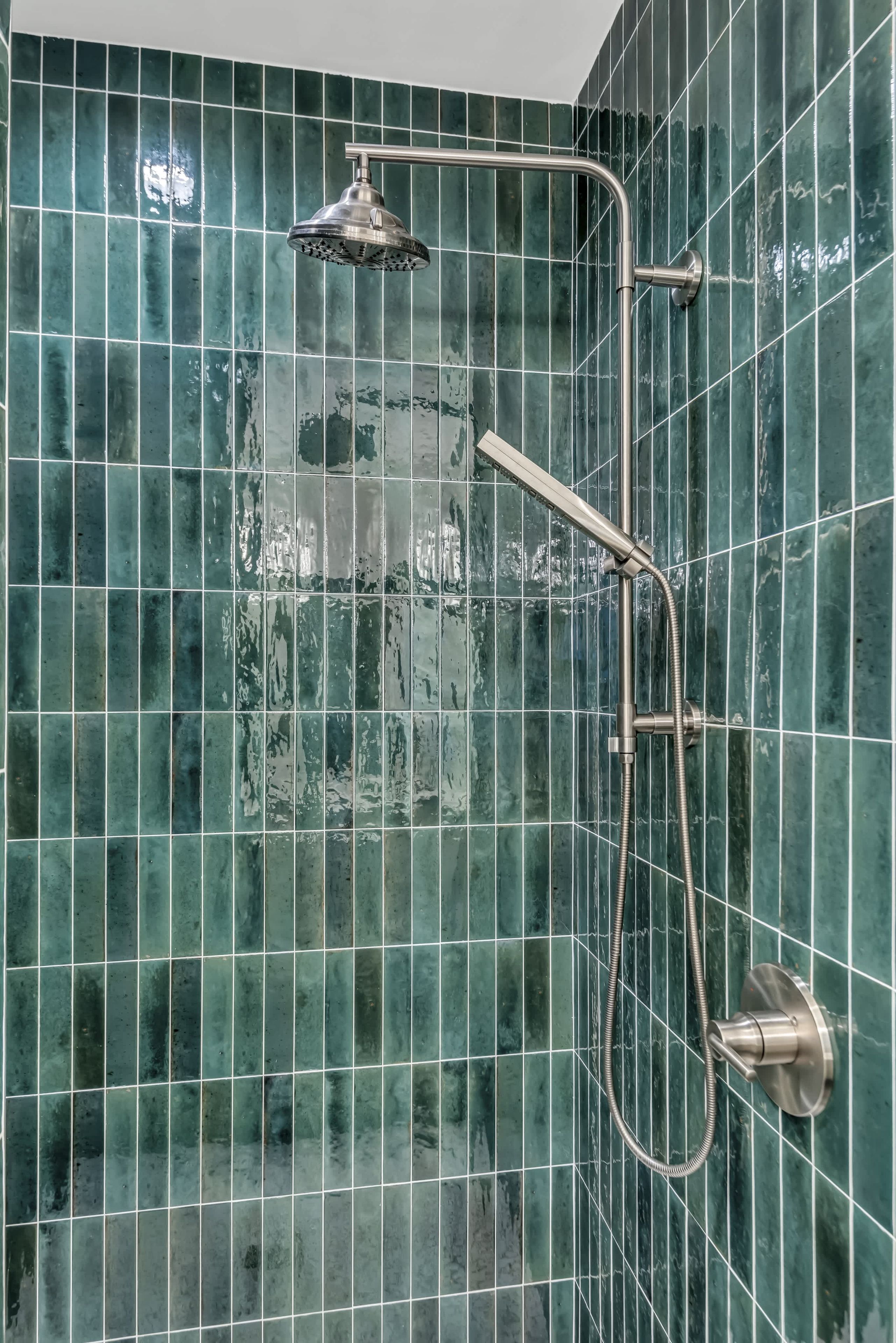 Eine Dusche mit Duschkopf und Handbrause vor einer gefliesten Wand.