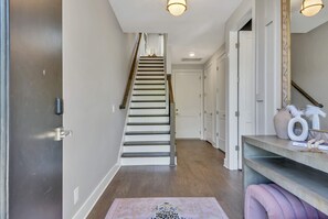 A hallway with a wooden staircase, white doors, and a light fixture above the staircase.