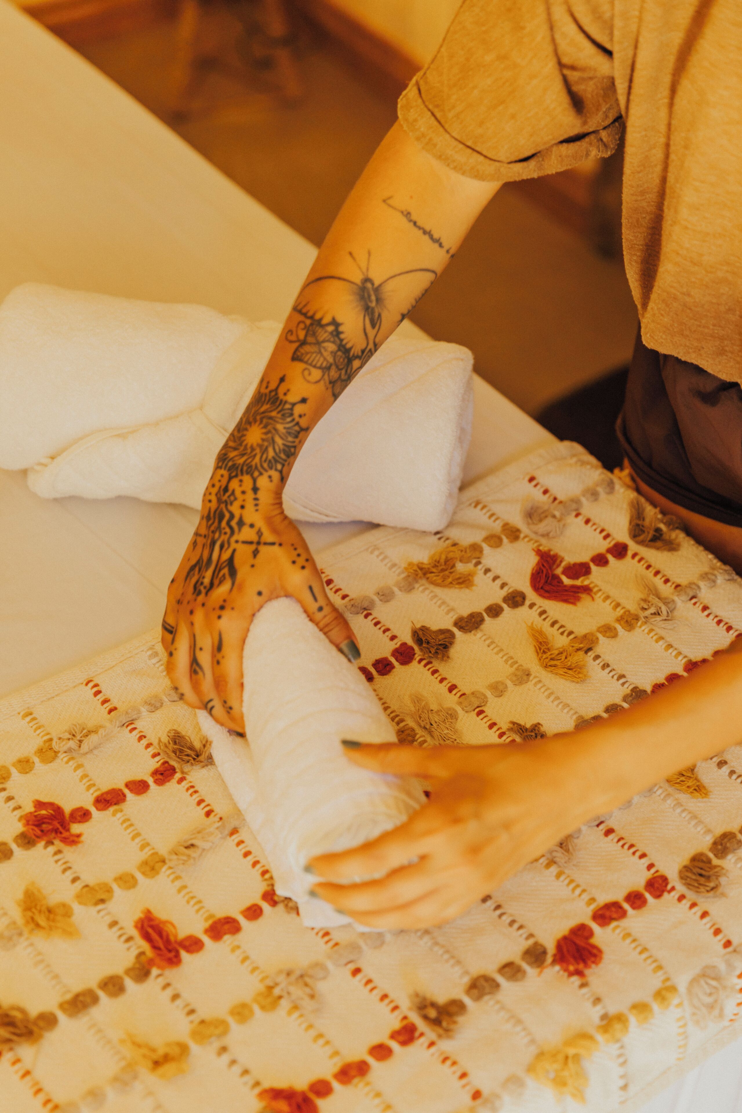 Una persona enrollando una toalla en el brazo, descansando sobre una cama con una colcha estampada de flores.