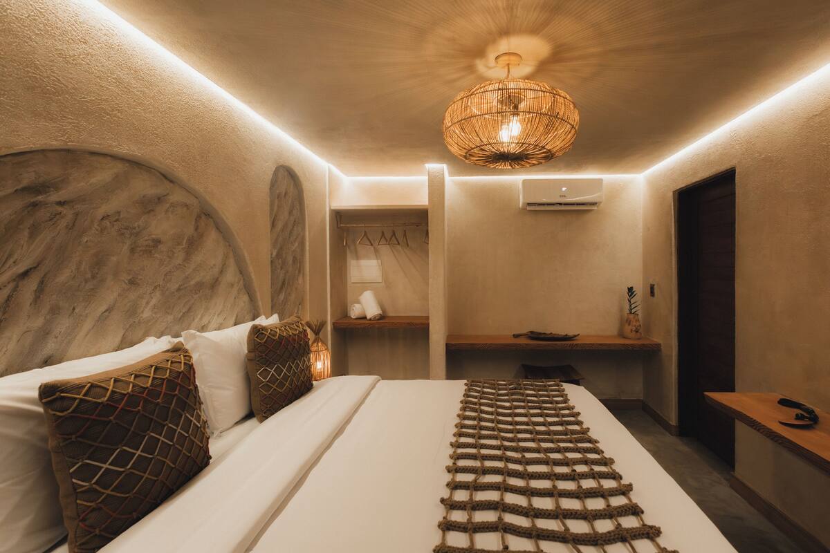 Un dormitorio moderno con cama, cabecero de madera, lámpara colgante tejida, mesita de noche y aire acondicionado instalado en la pared.