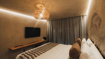 Quarto de hotel com cama grande, televisão de tela plana na parede, mesa de cabeceira de madeira e luminária de tecido.