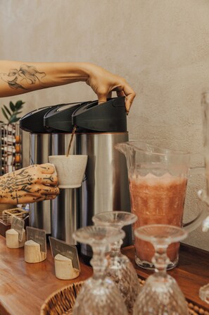 A coffee machine dispensing coffee into a cup, a pitcher of coffee, and a barista with tattoos. - Pousada Topázio by Amana (Fernando de Noronha)