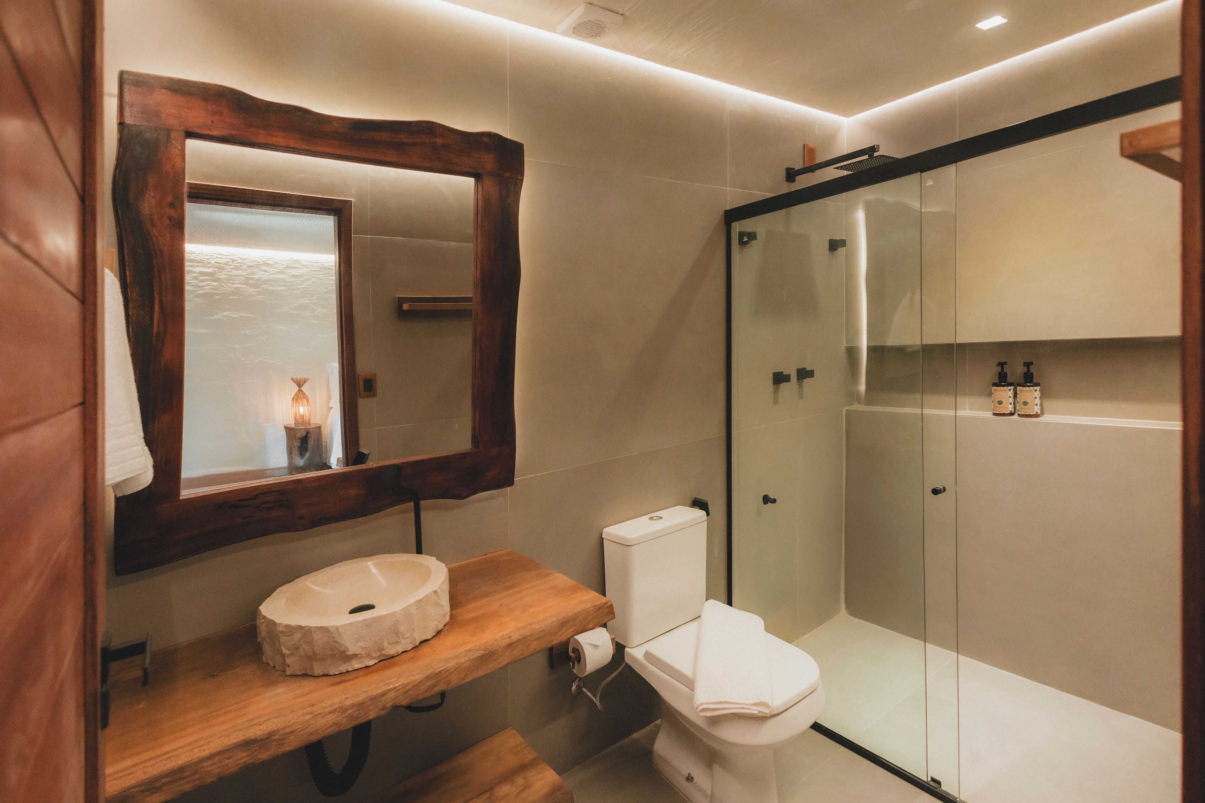 A modern bathroom with a wooden vanity, a toilet, a glass shower enclosure, and a mirror with a wooden frame.