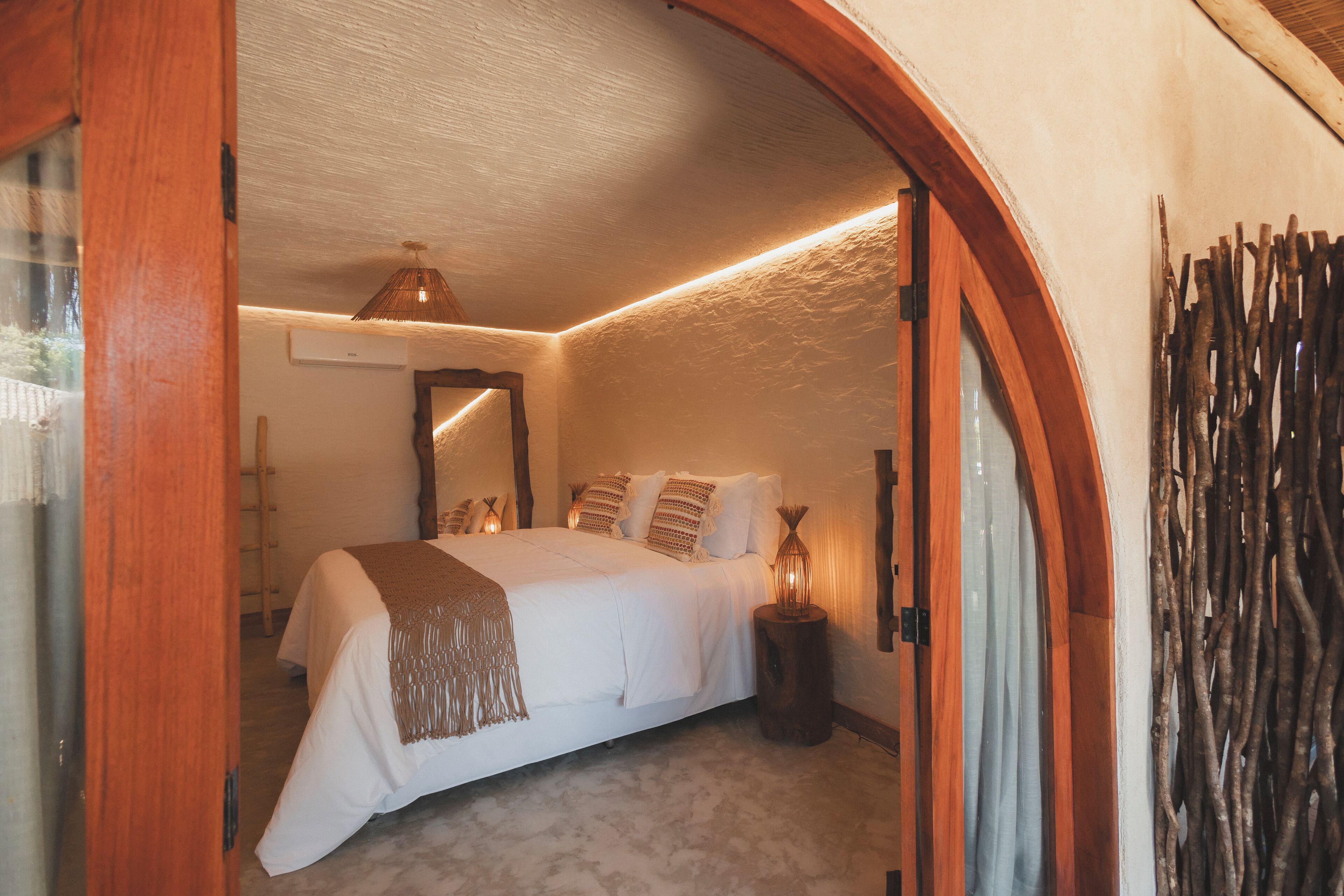 A bedroom with a large bed, a wooden door frame, a mirror, and a wall-mounted light fixture.
