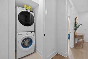 A laundry room with a front-loading washer and dryer, a small table with a plant, and a mirror on the wall.