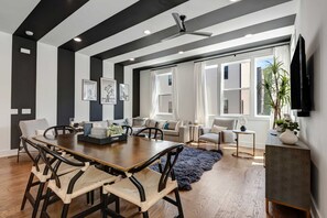 Un salon moderne avec un coin repas, de grandes fenêtres et un ventilateur de plafond.