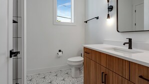 A modern bathroom with a white toilet, a wooden vanity, a large mirror, and a geometric-patterned floor.