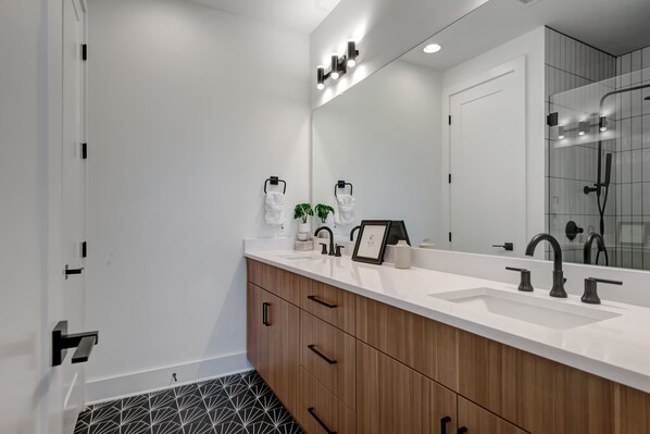 A modern bathroom with a large mirror, wooden vanity, and a shower area.