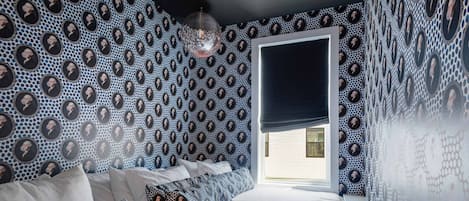 A bedroom with a patterned wallpaper, a bed with white bedding, and a window with a dark blind.