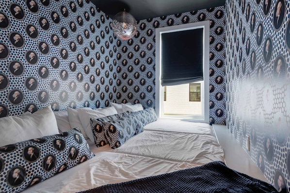 A bedroom with a patterned wallpaper, a bed with white bedding, and a window with a dark blind.