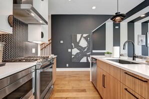 A modern kitchen with stainless steel appliances, a herringbone-patterned backsplash, a black and white abstract painting, and wooden cabinets.