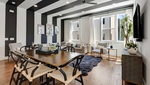 A modern living room with a dining area, large windows, and a ceiling fan.