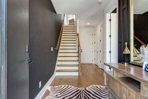 Un intérieur moderne avec un escalier en bois, un tapis à motifs zébrés et une console en bois surmontée d’une lampe.