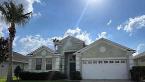 A two-story house with a garage, a front lawn, and a palm tree. - Near Disney 4Bd/3Ba Villa w/ Private Pool, Hot Tub in Gated Resort Community (Kissimmee)