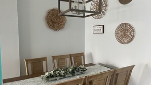A dining area with a wooden table, chairs, a decorative centerpiece, and wall decor including woven baskets and a sign. - Near Disney 4Bd/3Ba Villa w/ Private Pool, Hot Tub in Gated Resort Community (Kissimmee)