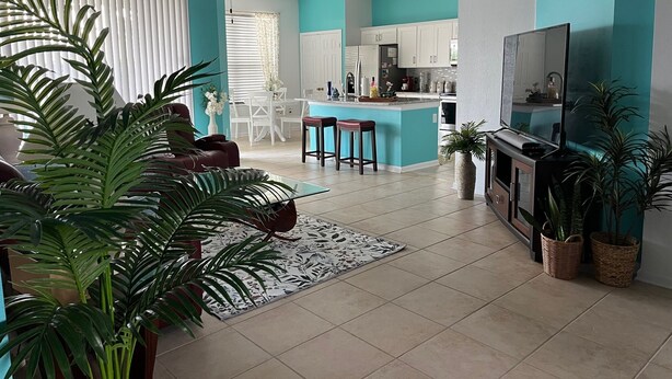A modern kitchen with white cabinets, a central island, and a dining area with a table and chairs. - Near Disney 4Bd/3Ba Villa w/ Private Pool, Hot Tub in Gated Resort Community (Kissimmee)