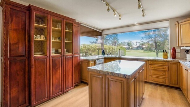 A spacious kitchen with wooden cabinets, a large island, and a view of the outdoors. - Prestigious Fairway Living – Luxe 2BR on 7th Hole, Mission Hills (Rancho Mirage)