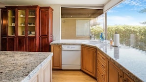 A kitchen with granite countertops, wooden cabinets, and a dishwasher. - Prestigious Fairway Living – Luxe 2BR on 7th Hole, Mission Hills (Rancho Mirage)