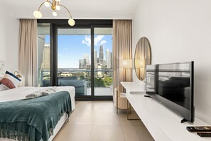 A hotel room with a bed, a desk, a television, and a view of a city skyline through a large window. - Burj Vista - Prime Downtown Dubai (Dubai)