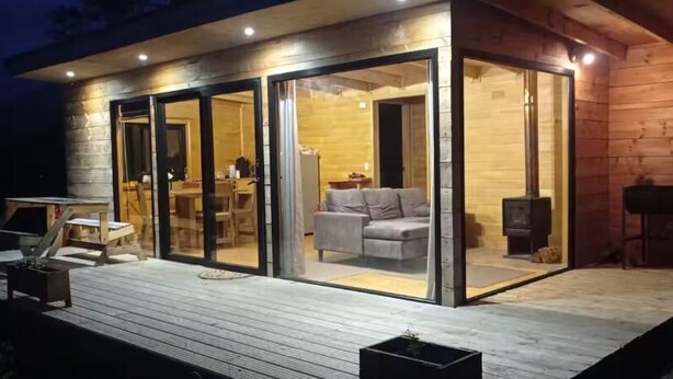 A modern log cabin with a glass-enclosed living area, a deck, and a fireplace. - Untamed Refuge in Rio Puelo (Arrayan) (Los Lagos)