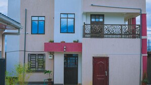 A two-story building with a red door, potted plants, and a paved courtyard. - Lux Suites Lions Den Holiday Homes (Nakuru)