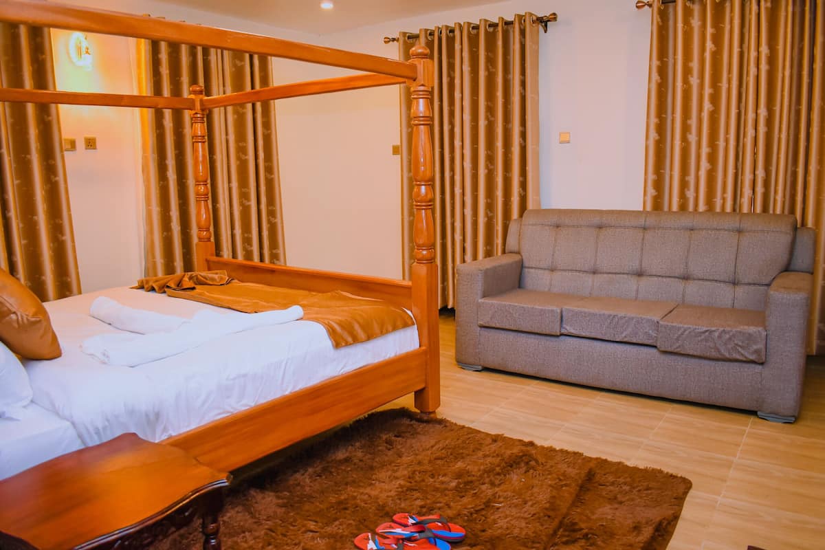 Een slaapkamer met een hemelbed, een grijze bank en een bruin vloerkleed.