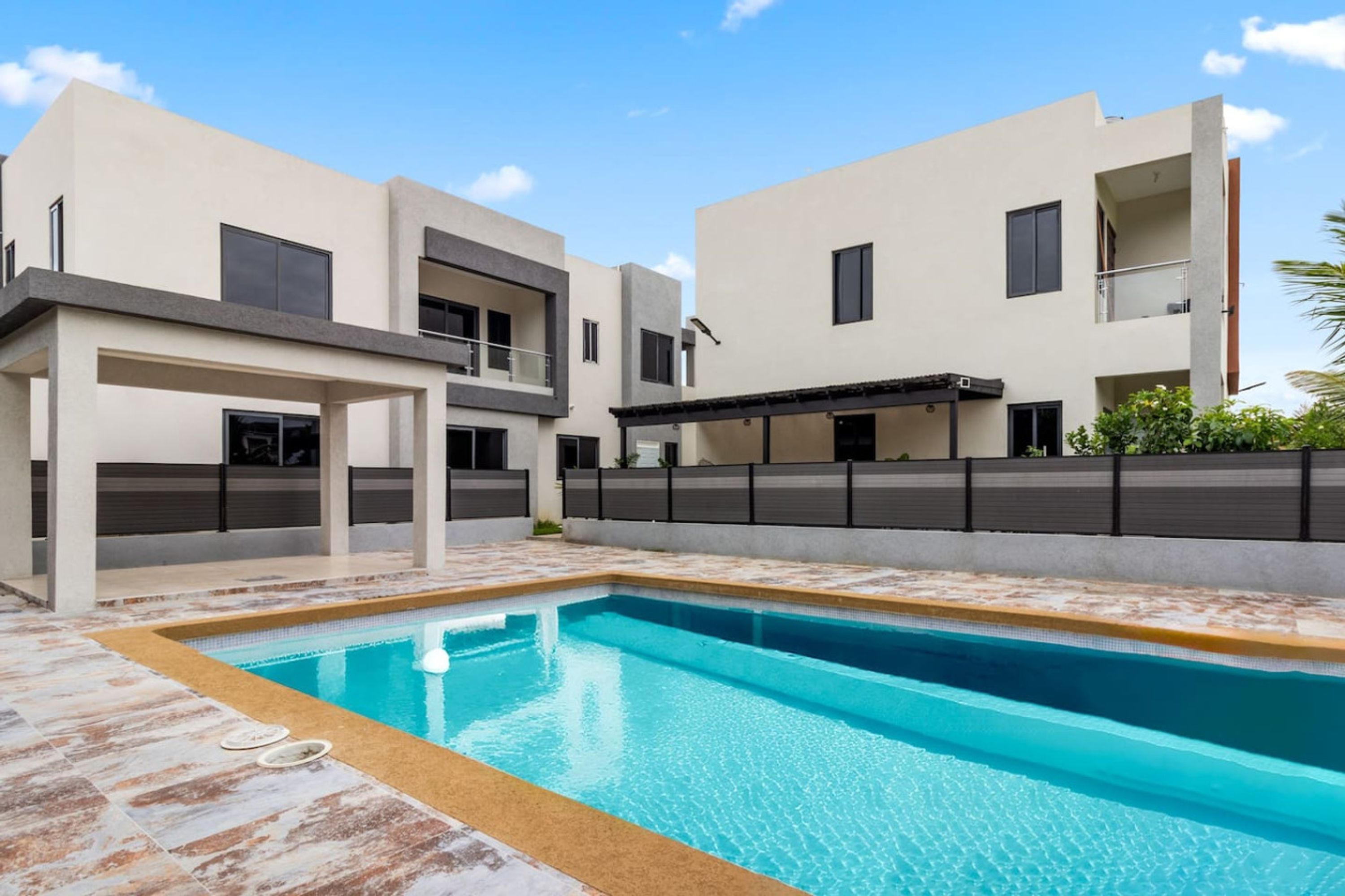 A modern pool area with a rectangular pool, a covered seating area, and a multi-story building with balconies.