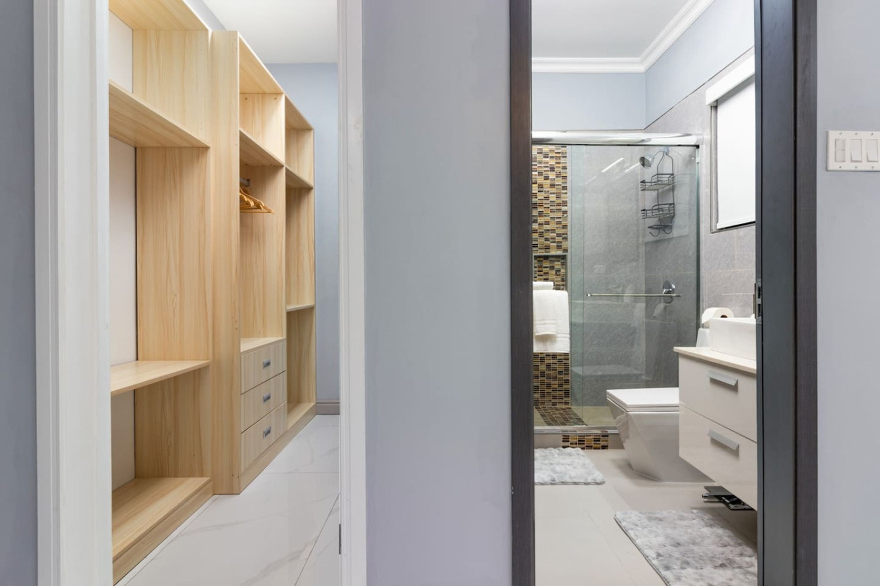 Un baño moderno con ducha de vidrio, tocador de madera y vestidor.