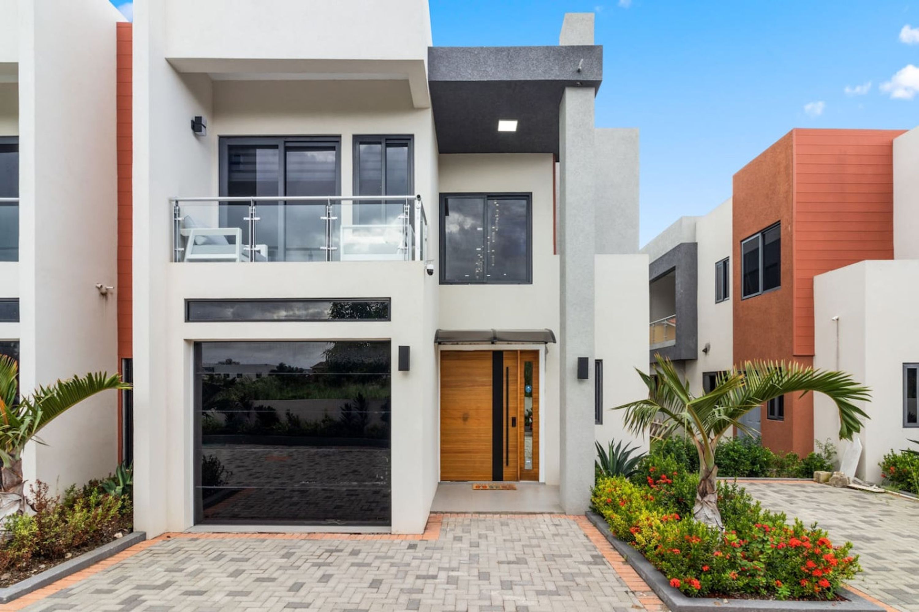 A modern two-story residential building with a balcony, large windows, and a well-maintained garden.
