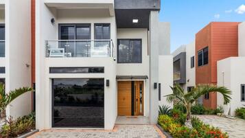 A modern two-story residential building with a balcony, large windows, and a well-maintained garden.