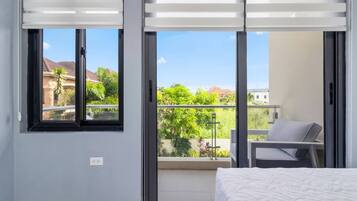 A bedroom with a bed, a balcony with a chair, and a view of greenery and buildings.