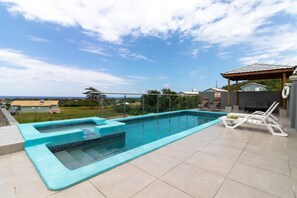 A swimming pool with a hot tub, surrounded by a tiled deck and lounge chairs.
