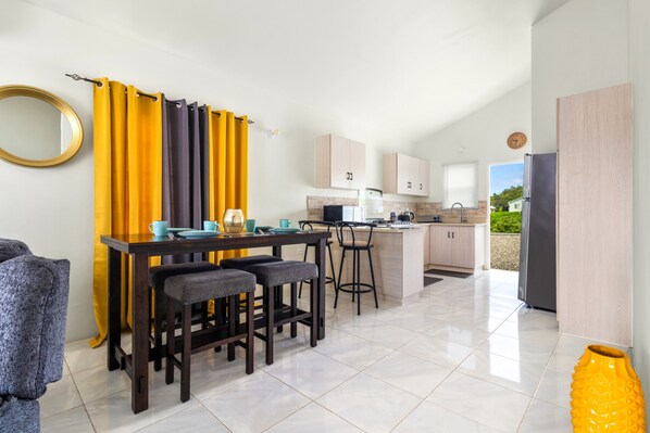 A modern kitchen with a dining area, featuring a kitchen island, bar stools, and a yellow curtain.