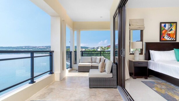 Un balcon avec vue sur la mer et un lit avec une table de chevet et un tableau.