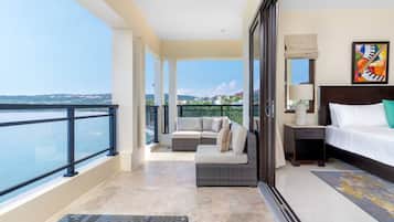 A balcony with a view of the sea and a bed with a nightstand and a painting.
