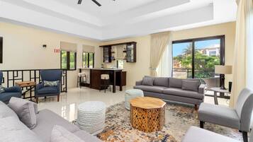 A spacious living room with a modern sofa, armchairs, a wooden coffee table, and a dining area with a bar.
